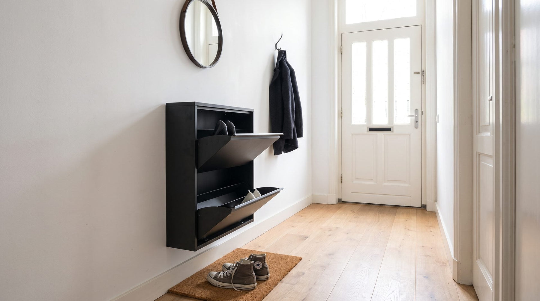 Zwarte stalen schoenenkast met kantelvakken aan de wand in een smalle hal