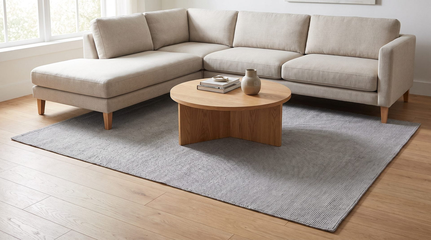 Grijs wollen vloerkleed onder een lichte hoekbank met ronde salontafel