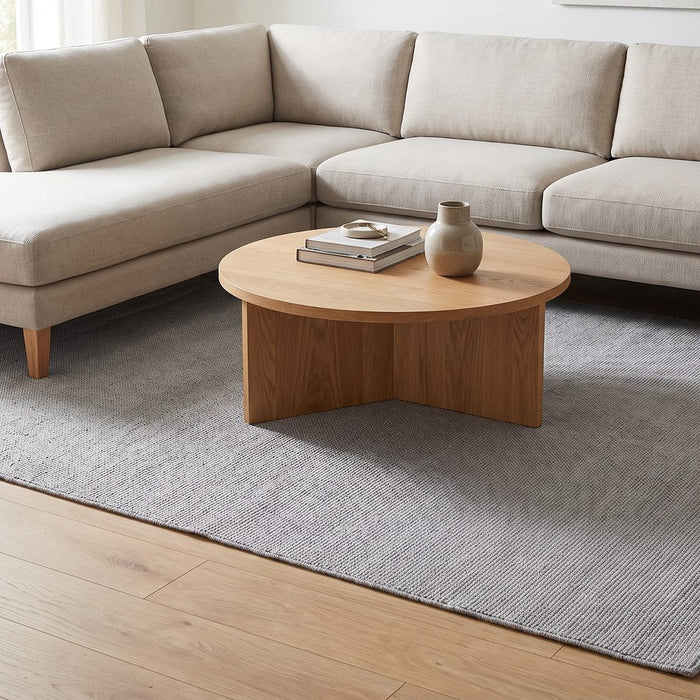 Grijs wollen vloerkleed onder een lichte hoekbank met ronde salontafel
