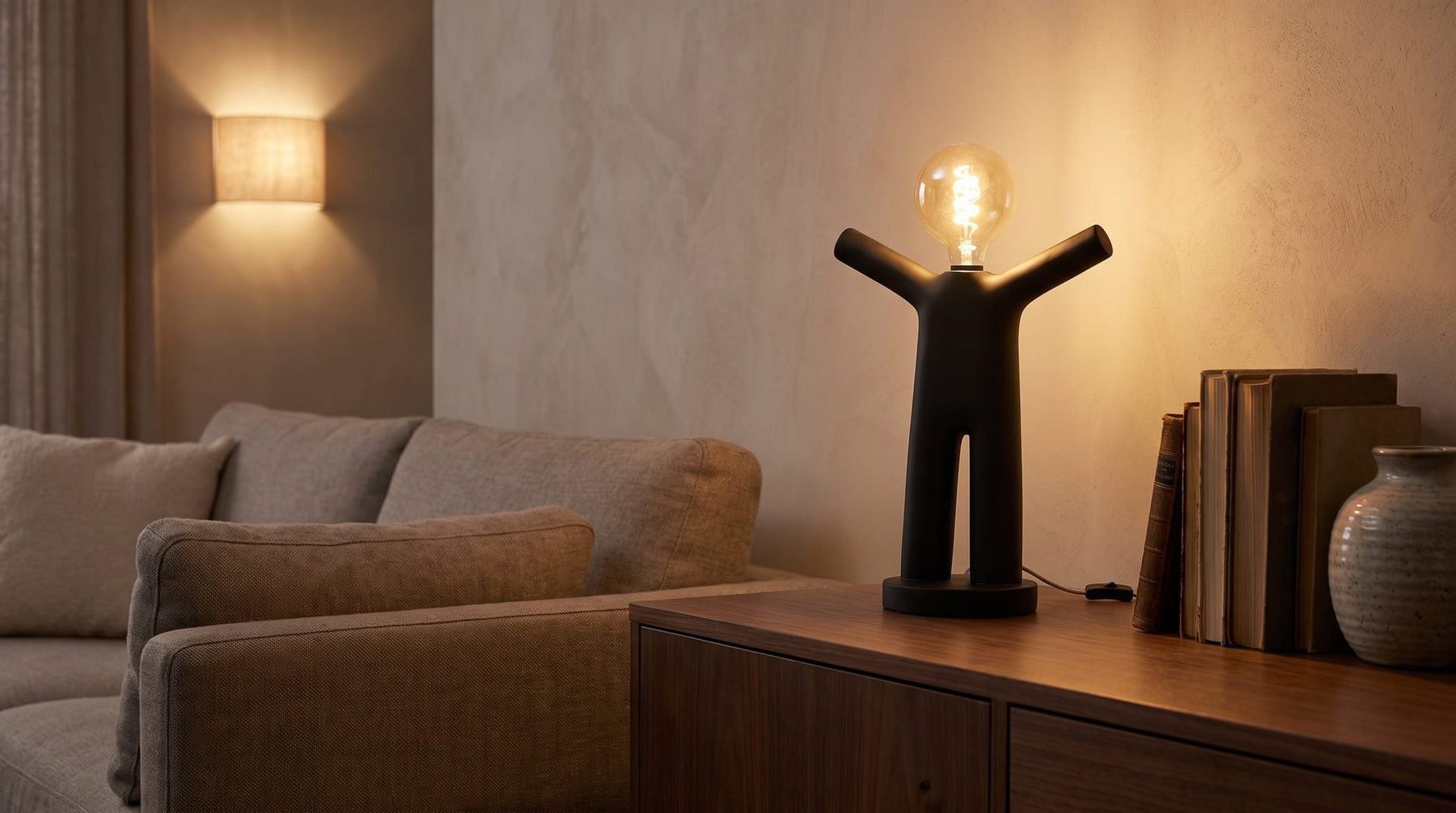 Zwarte tafellamp op een dressoir naast de bank, met een wandlamp op de achtergrond