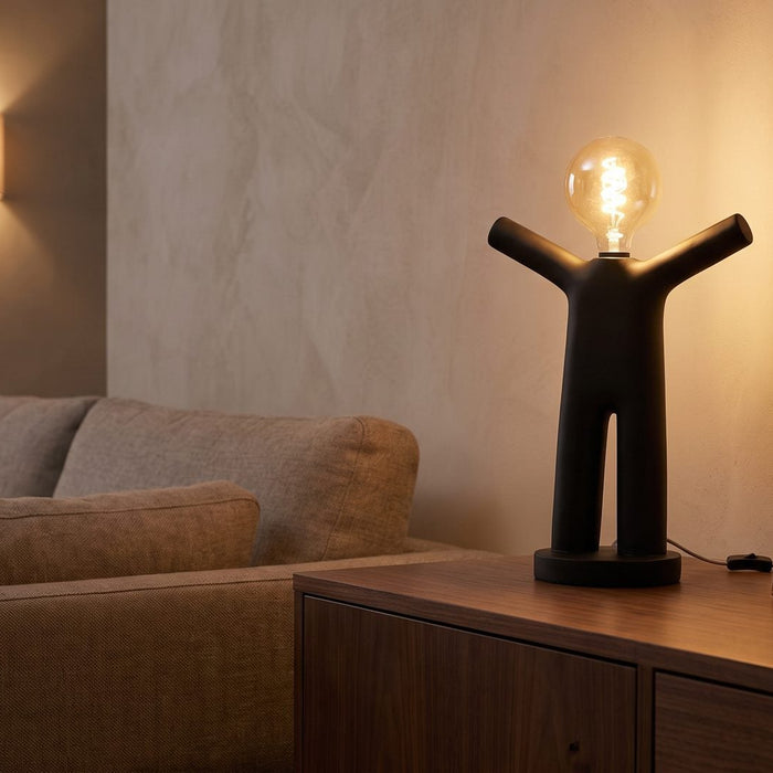 Zwarte tafellamp op een dressoir naast de bank, met een wandlamp op de achtergrond