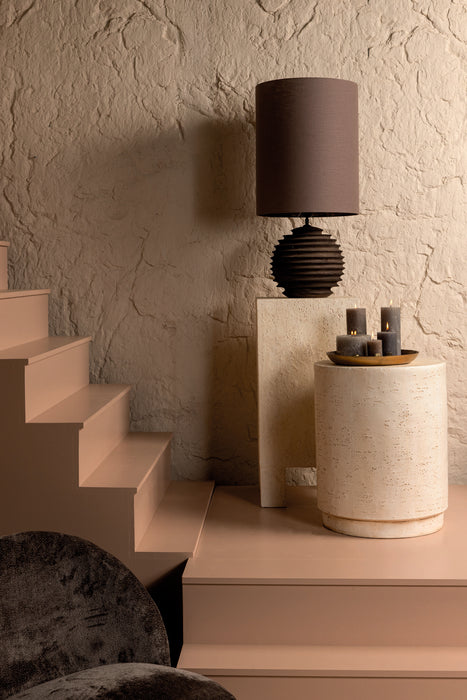 Crème kleurige, ronde bijzettafel van beton met een robuuste textuur, geplaatst in een sfeervol interieur.