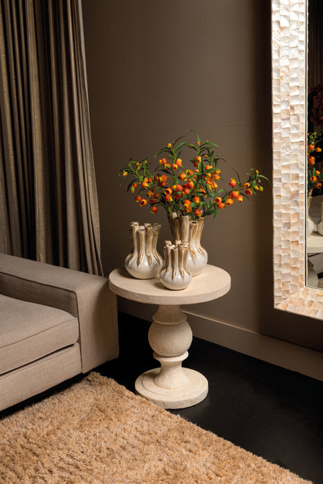 Ronde crème bijzettafel Muza van PTMD in beton met een decoratieve voet, geplaatst in een sfeervol interieur.