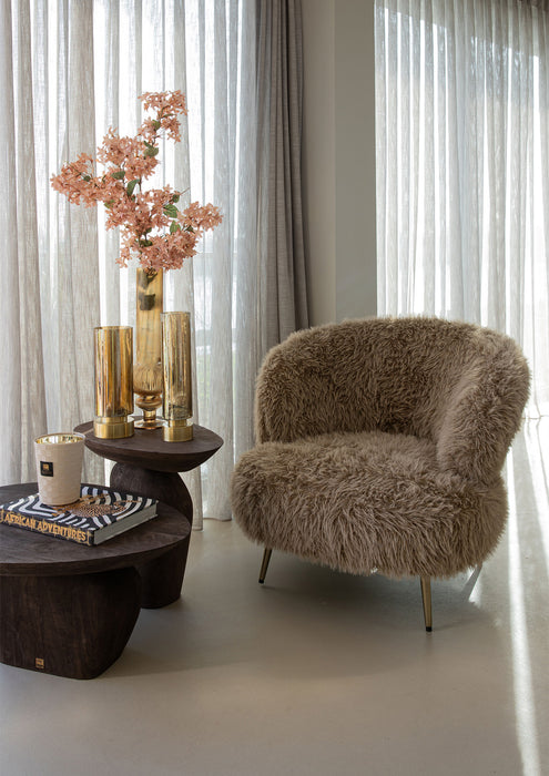 Bruine fauteuil Franklyn van PTMD met aaibare polyester bekleding en een slank metalen onderstel in een sfeervol interieur.