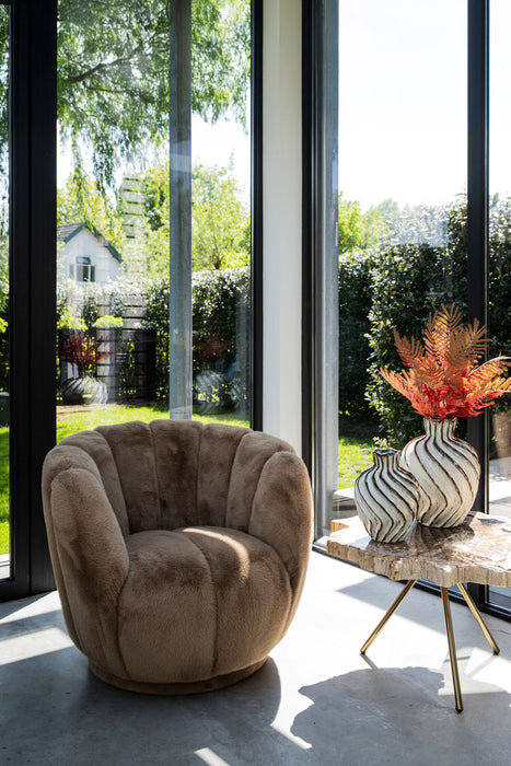 PTMD Furia fauteuil in mocca polyester met zachte bontachtige textuur en ronde vormen bij een raampartij.