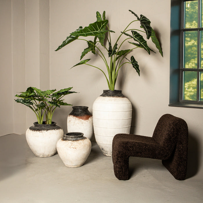 Moderne koffiebruine fauteuil van polyester met een gestructureerde bekleding naast decoratieve witte vazen met planten.