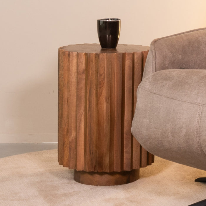LABEL51 Novan bijzettafel van glad mangohout met een geribbeld design, 35 cm breed, naast een grijze fauteuil.